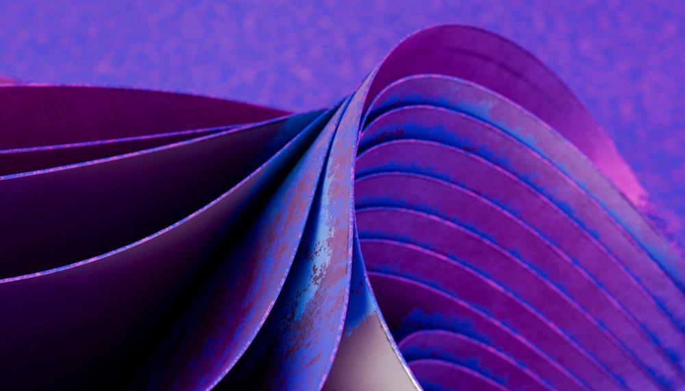 Folded sheets of blue and purple paper creating an abstract and artistic texture with curved edges and layered patterns.
