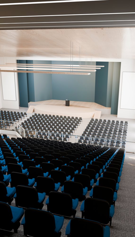Conference hall with stage, podium, and rows of empty blue and black chairs in a spacious auditorium.