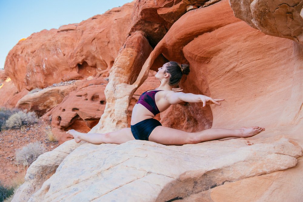 Woman performs a yoga split pose on natural red rock formations outdoors in the USA under a clear sky.