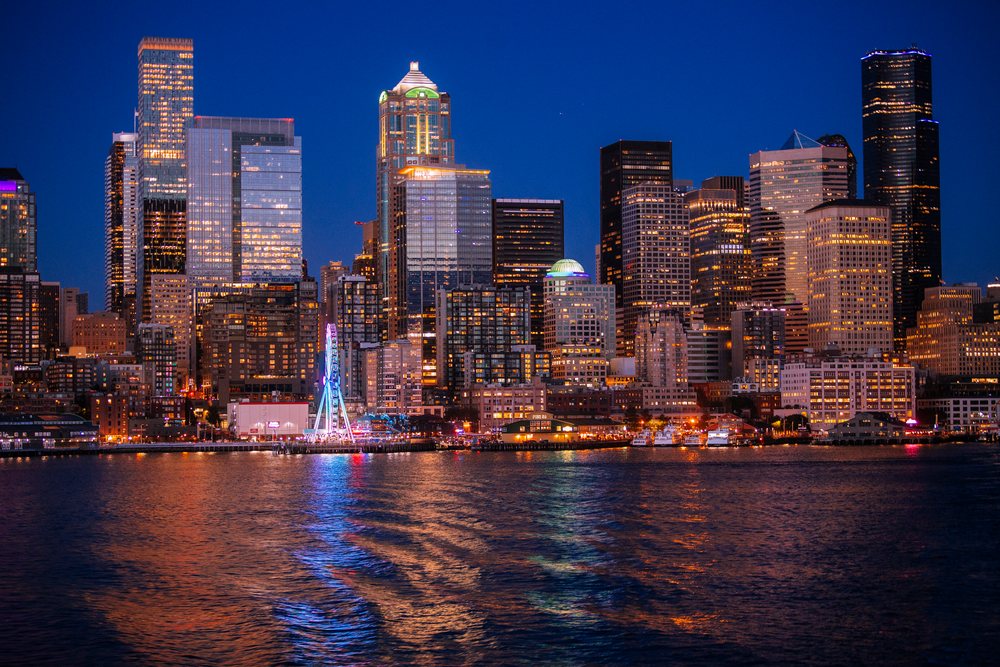 Nighttime Seattle skyline with colorful illuminated skyscrapers and a Ferris wheel reflecting on the waterfront, WA, USA.