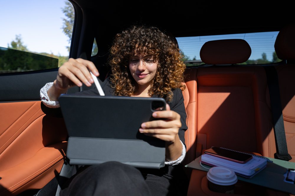 Businesswoman working remotely using a tablet with digital pen inside a car near Spain during the daytime, remote work, businesswoman, car.