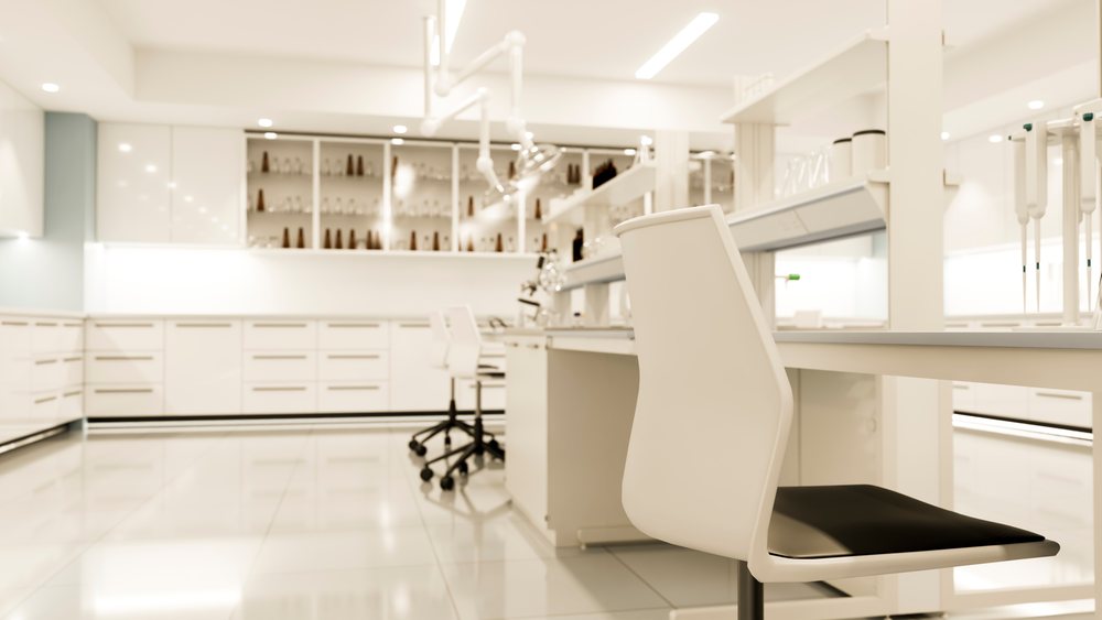 Modern laboratory interior with white chairs, lab benches, scientific instruments, and bright overhead lighting in a sterile environment.