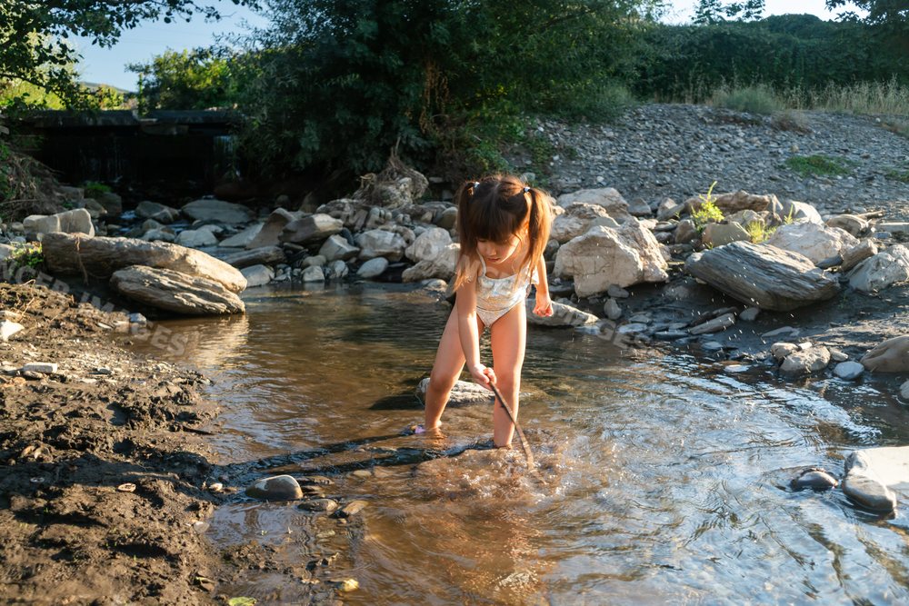 A young white child playing with a stick in a shallow creek outdoors