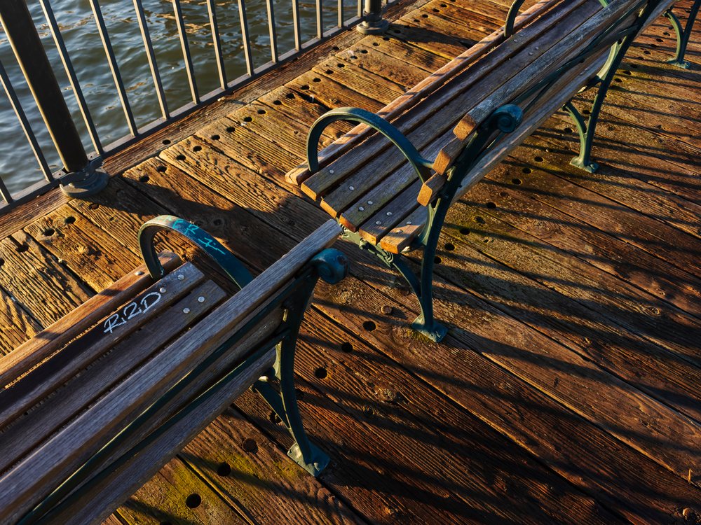 Two wooden benches with metal armrests rest on a weathered Pier beside water at Sunrise along the Embarcadero, landscape, cityscape, city life, San Francisco, California, USA.