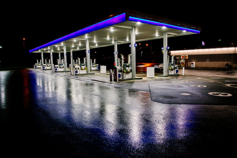 Gas station at night, showing illuminated fuel pumps under a canopy with wet pavement reflecting lights, Tacoma, WA, USA.