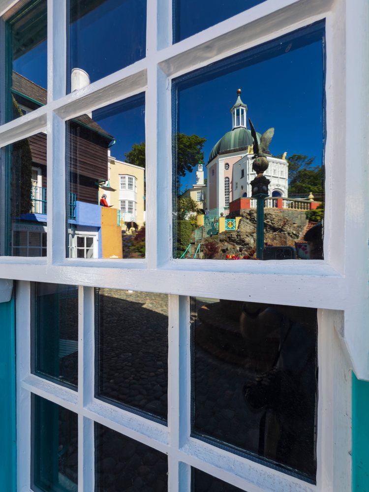 Reflection of Italianate domed buildings, sculpture, and cobblestone pavement in a white-framed window, Landscape, Portmeirion, Gwynedd, Wales.