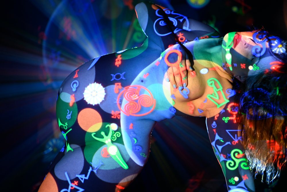 Artistic nude female body with colorful symbolic light projections and rays on bare skin in a dark setting, pregnancy.