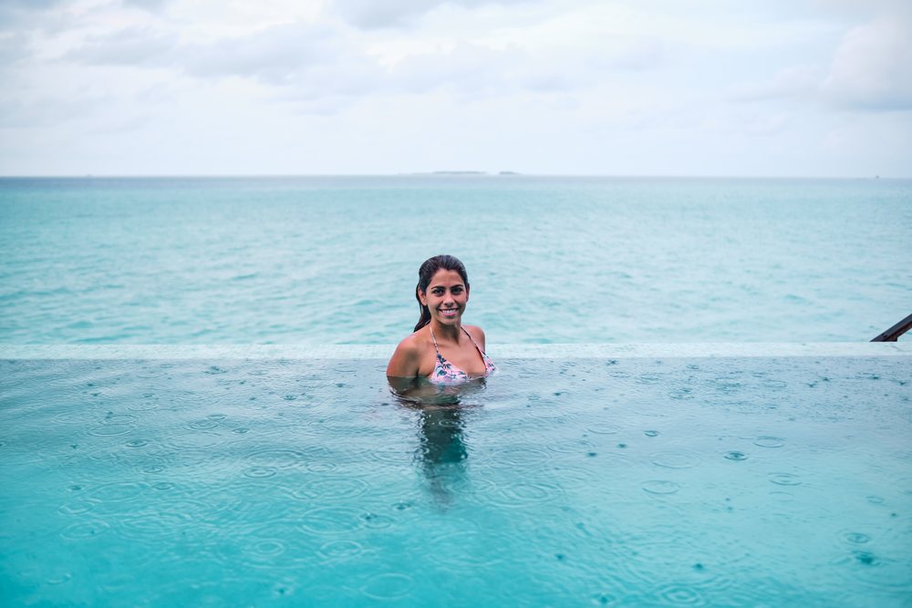 A white woman swimming in an infinity pool overlooking the ocean