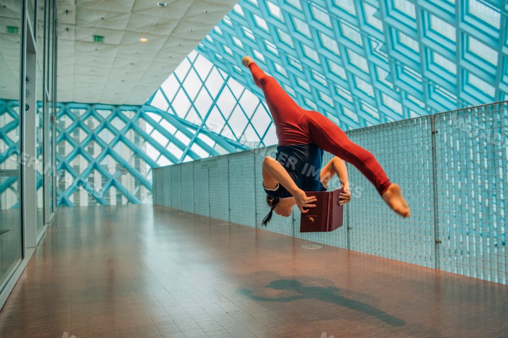 Woman jumping and reading a book in a library