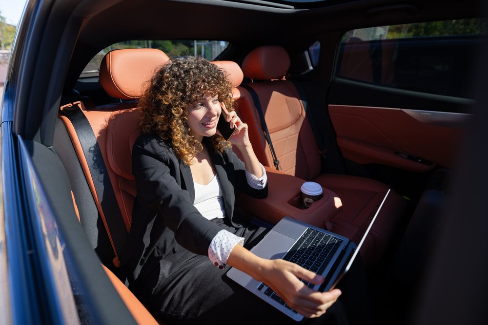 Businesswoman working remotely on laptop and talking on phone in the backseat of a car in Spain during daytime, remote work, businesswoman, car.