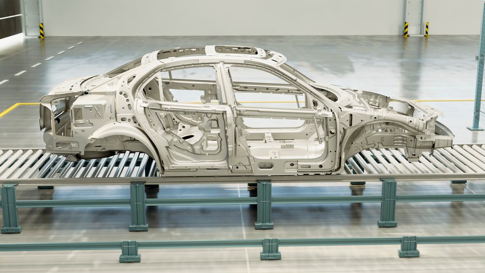 Car body shell on conveyor rollers inside an industrial automotive manufacturing workshop.