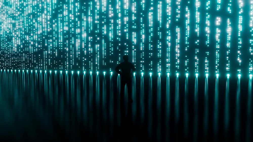 Silhouette of a person standing with hands on hips amid vertical glowing light dots in a dark digital installation space.