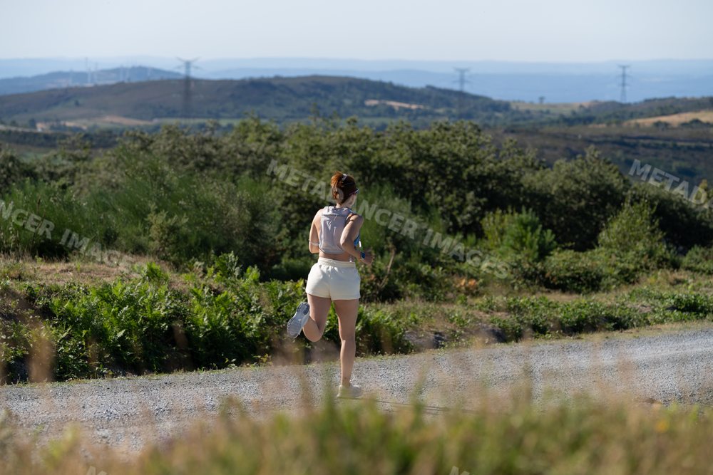 A white woman runs on a rural trail surrounded by greenery in Galicia