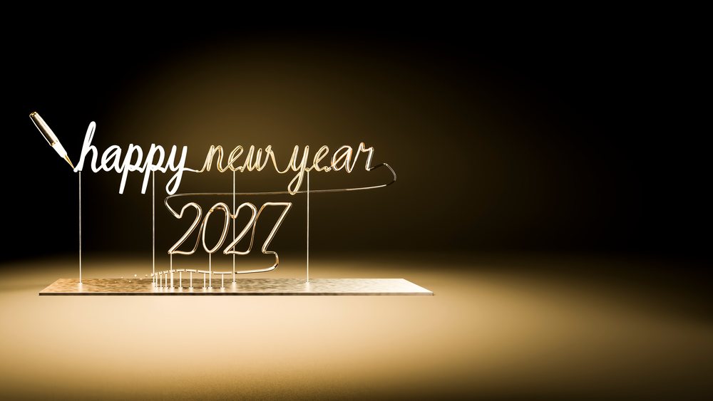 Gold wire forming the script text 'happy new year 2027' with a pen on a glowing black gradient background.