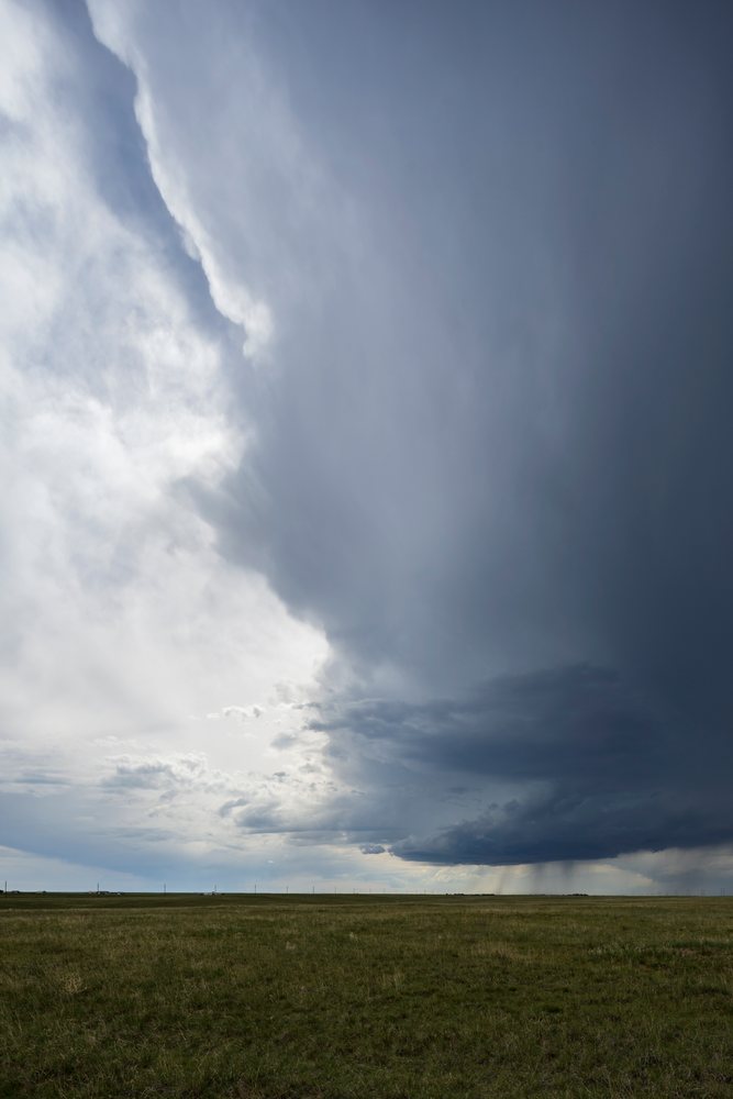 Developing Supercell storm cloud develops over a grass field with visible rain and power lines, Cheyenne, Wyoming, USA.