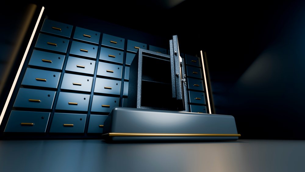 Open safe deposit box with metal door open in a dark bank vault room.