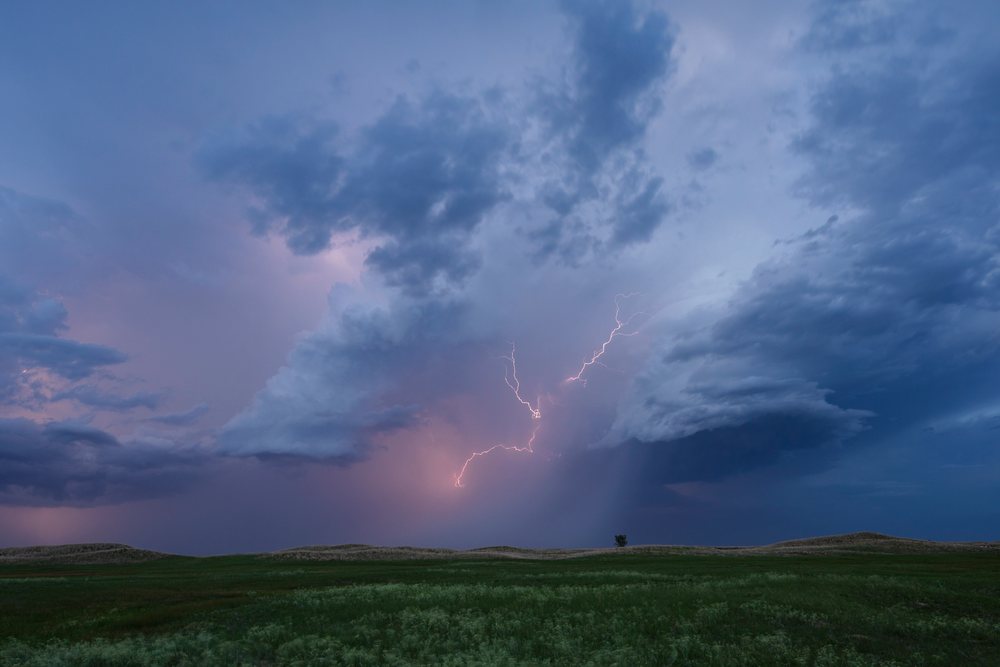 Lightning strikes over green grassy hills in the Nebraska Sandhills during Blue Hour with storm clouds overhead, Storm Chasing, Weather, Environmental Issues, Dunning, USA.