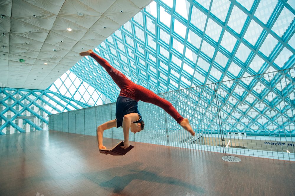 A woman doing a handstand split reading a book in a library