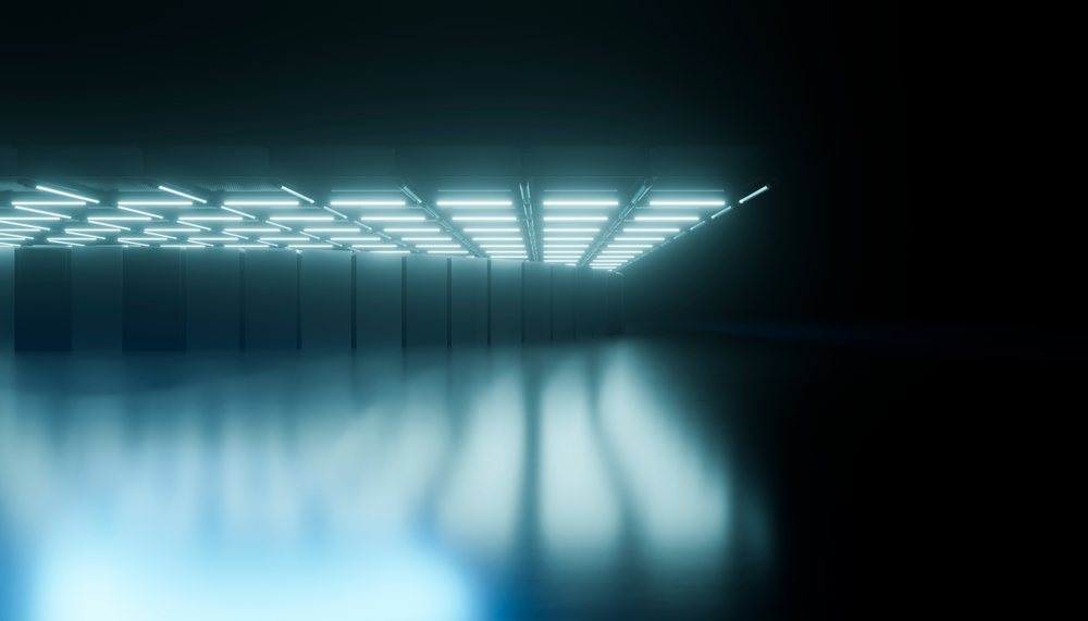 Data center with rows of server racks illuminated by overhead LED lights reflecting on the floor in a dark technology room.