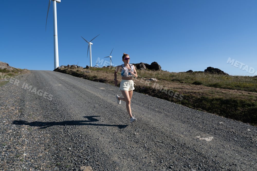 A white woman jogging on a gravel road near wind turbines in Galicia