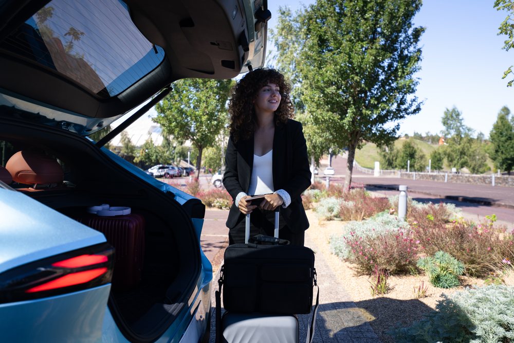 Businesswoman with luggage standing by an open car trunk in a sunny parking lot, Business Travel, Spain.