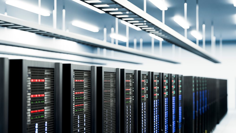 Rows of black server racks with front mesh panels and multiple colored LED indicator lights in a modern indoor data center technology room.
