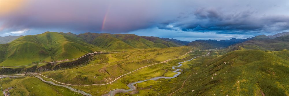 Rainbow arcs over green hills and winding river at sunset in Kham Tibet, Zhuqingcun, Sechuan Province, People's Republic of China.