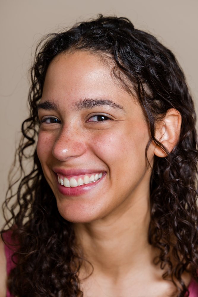 Close-up portrait of a cheerful woman with curly hair and freckles smiling against a neutral background, beauty shoot, Spain.