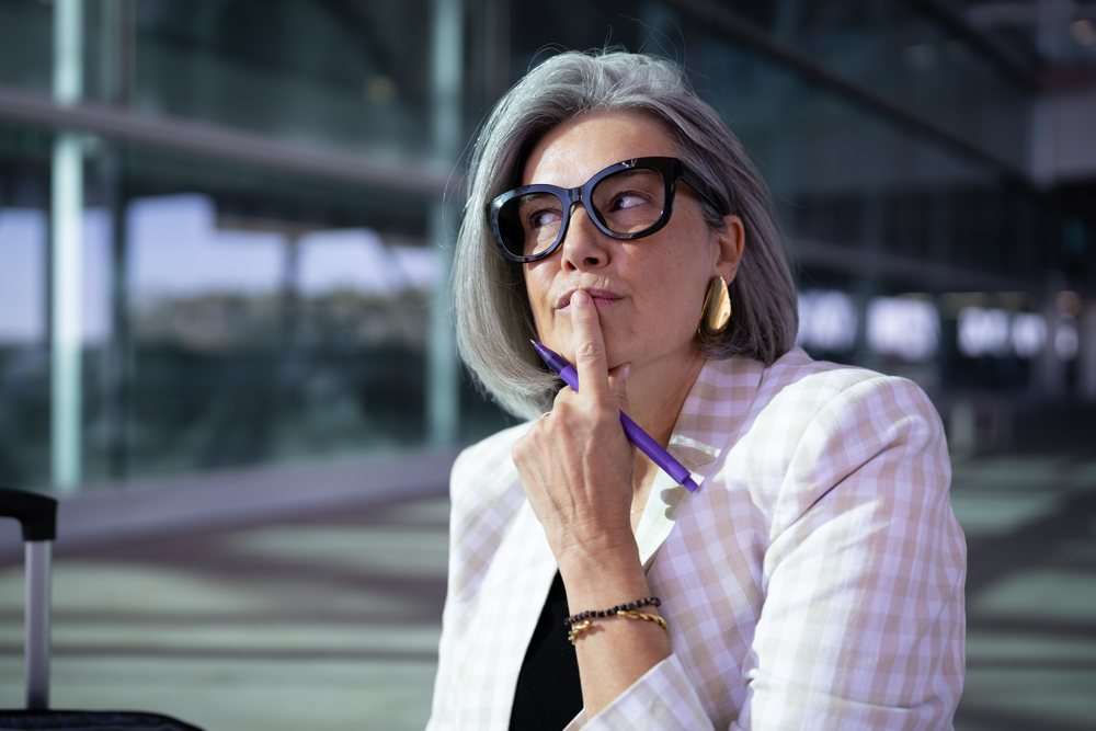 Businesswoman with gray hair and glasses holding a purple pen in an outdoor urban setting, Spain, Madrid.