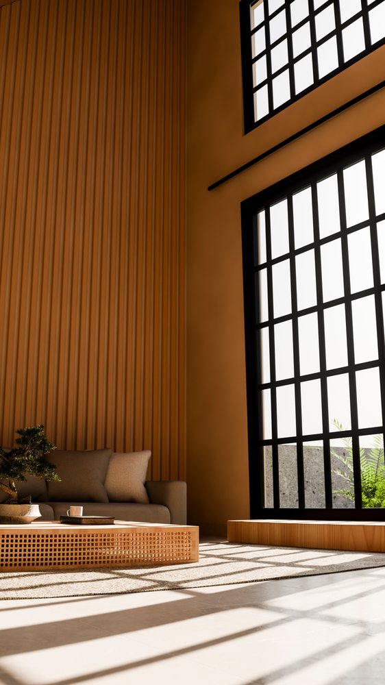 Modern living room with a large window casting shadows across a sofa and wooden coffee table holding a bonsai tree.