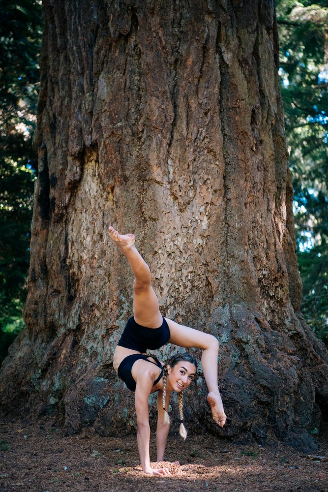 Young woman with braided hair performing an advanced handstand pose outdoors in a forest, contortionist, Tacoma, WA, USA.