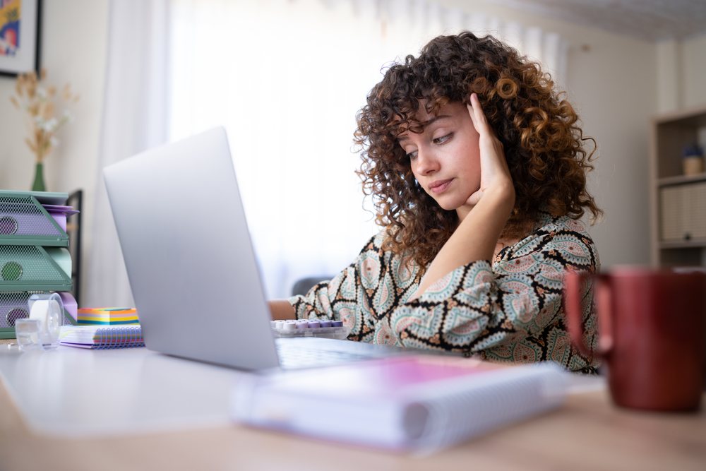Woman with curly hair working on a laptop at a desk in a home office, Spain.