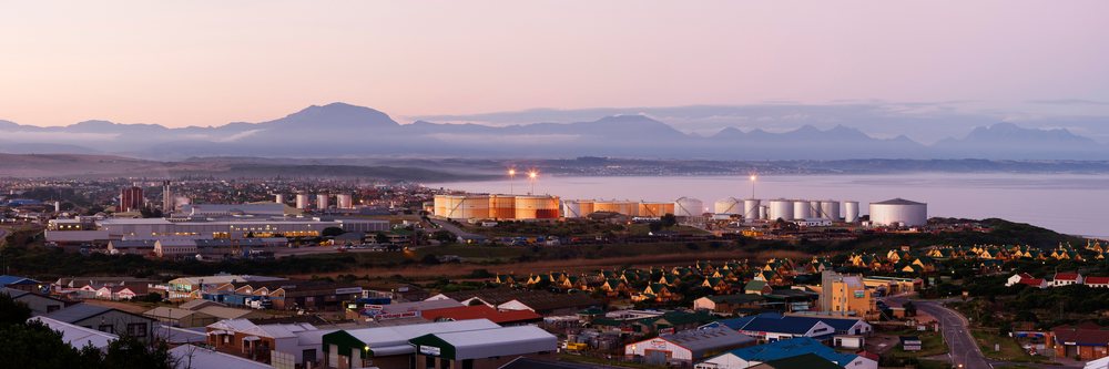 Mossel Bay skyline with industrial tanks near calm water and mountains, Dusk, Western Cape, South Africa.