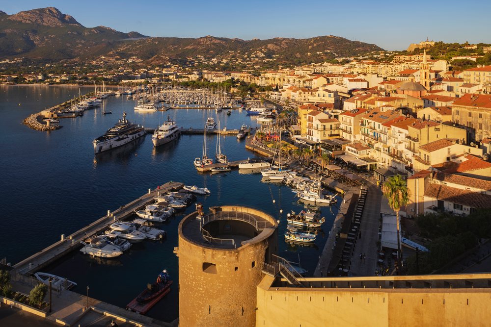 Harbour with boats docked in the water beside the city and mountains in the background at sunset, Travel Photography, Calvi, Corsica, France.