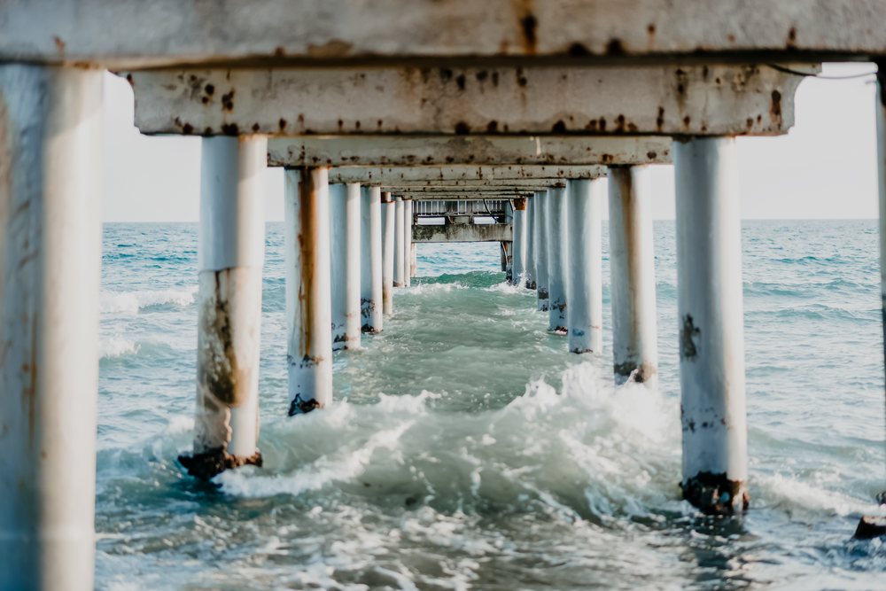View under a rusted pier with ocean waves crashing against pillars at the coast of, Spain.