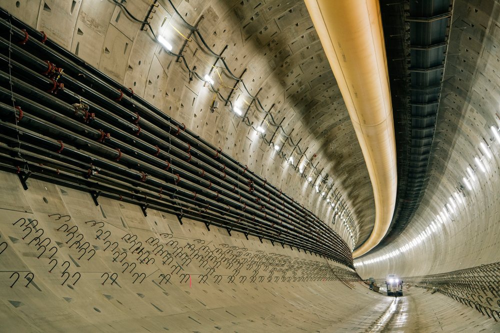 Interior view of a tunnel under construction showing concrete walls, utility pipes, and a construction vehicle, Bertha, drilling, USA.