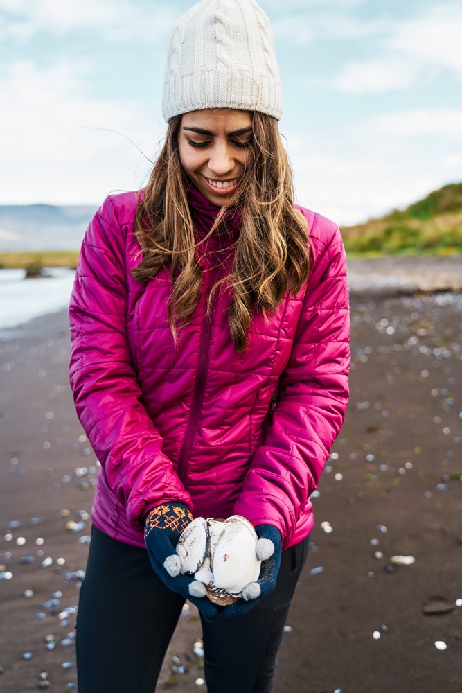 A white woman holds seashells on a beach in Iceland enjoying nature