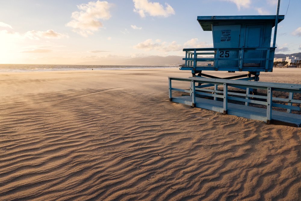 Lifeguard tower number 25 stands on the sandy Venice Beach shore at sunset with ocean waves and clouds in the sky, CA, USA.