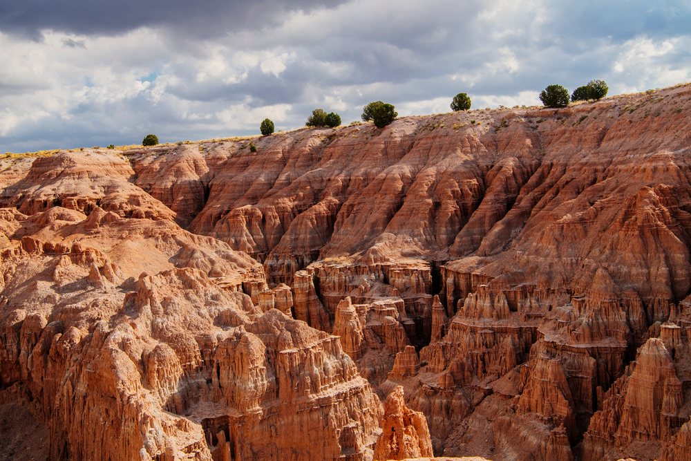 Cloudy sky over red rock formations, cliffs, and scattered trees, Cathedral Gorge State Park, Nevada, USA.