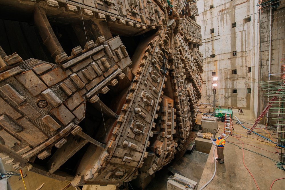 Two construction workers in safety gear inspect a massive tunnel boring machine inside an underground construction site, a massive tunnel boring machine, drilling, USA.