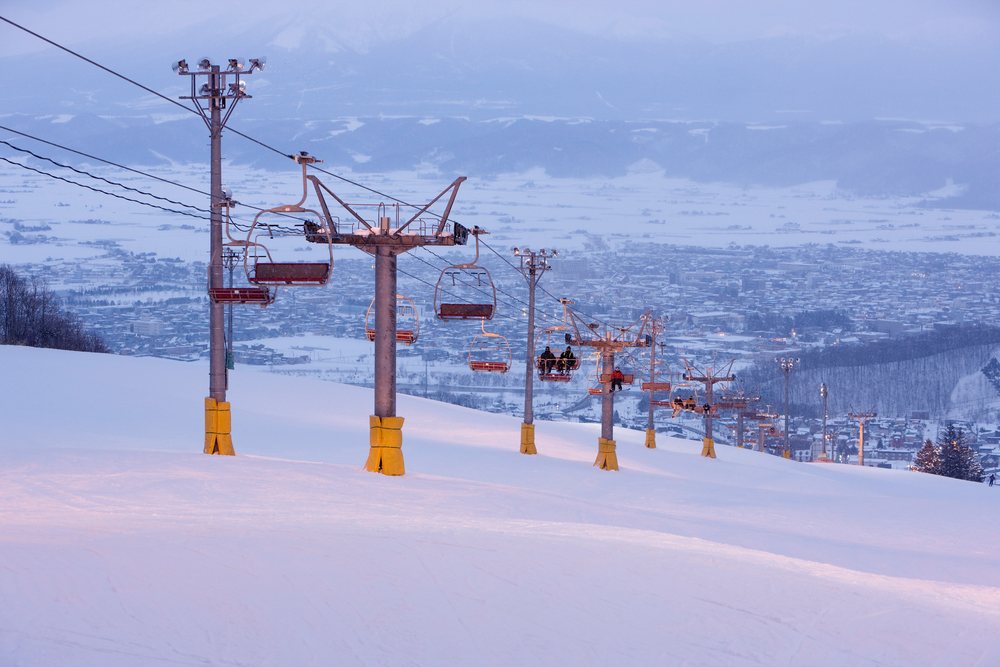 Ski lift with skiers ascending a snowy slope overlooking, Furano, Hokkaido, Japan.