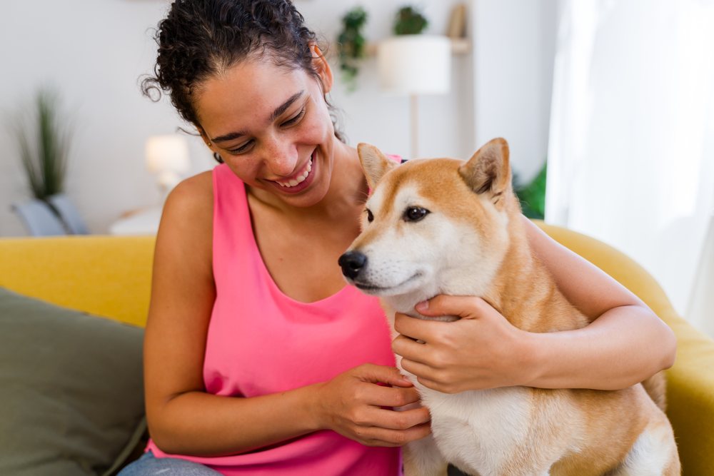 A woman affectionately pets her dog while sitting on a yellow couch in a cozy indoor living room, Spain.