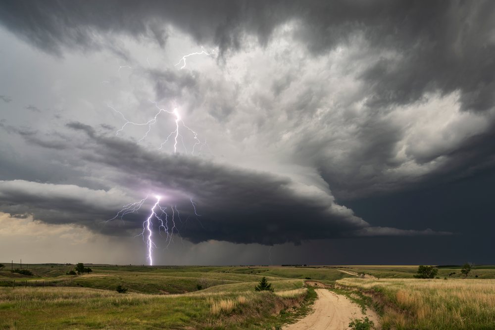 Lightning strikes from a dark cumulonimbus storm cloud over a rural dirt road in the grasslands, Wallace, Nebraska, USA.