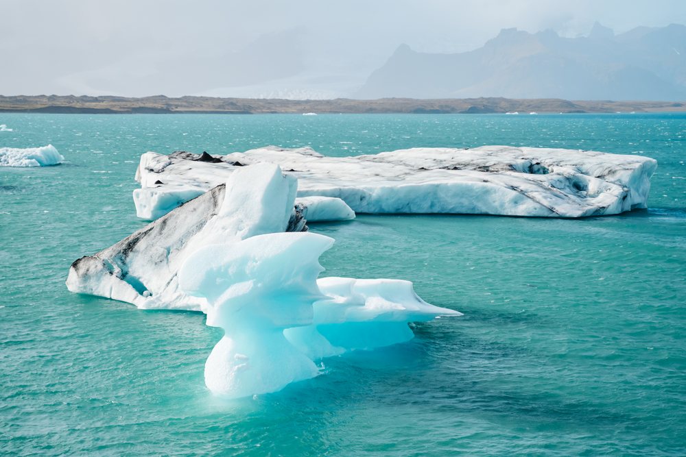 Large icebergs float in a turquoise glacial lake surrounded by distant icy terrain, Iceland.