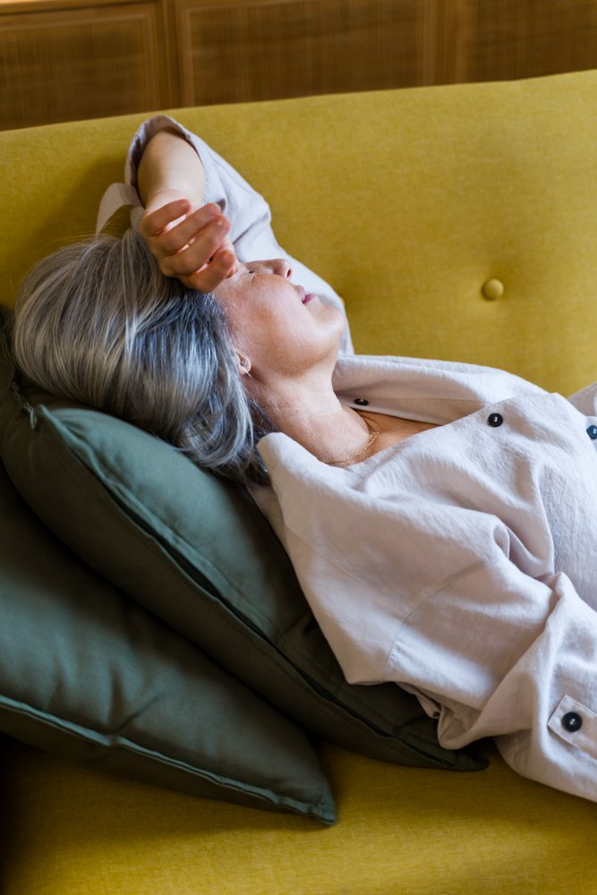 Woman with gray hair resting on a yellow sofa with green cushions indoors, Spain.