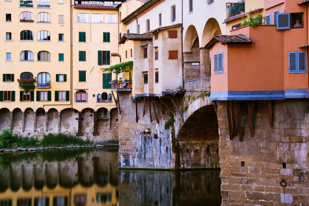 Medieval Ponte Vecchio stone arch bridge with historic buildings over River Arno, Italy reflecting in the water, Tuscany.
