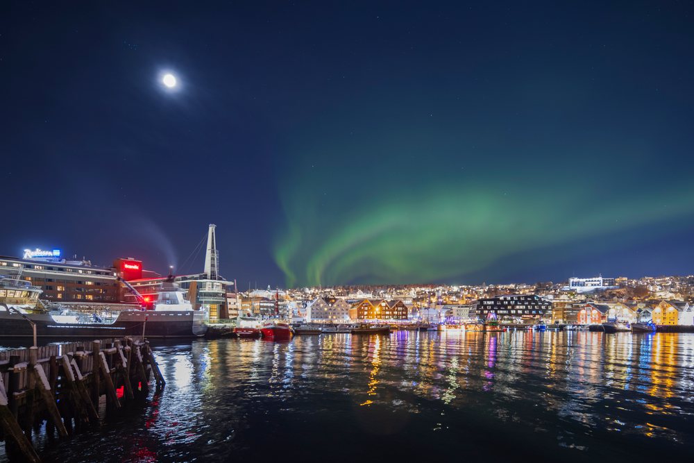 Northern Lights illuminate the night sky over the cityscape and harbor, with reflections on the water, Landscape, Tromsø, Norway.