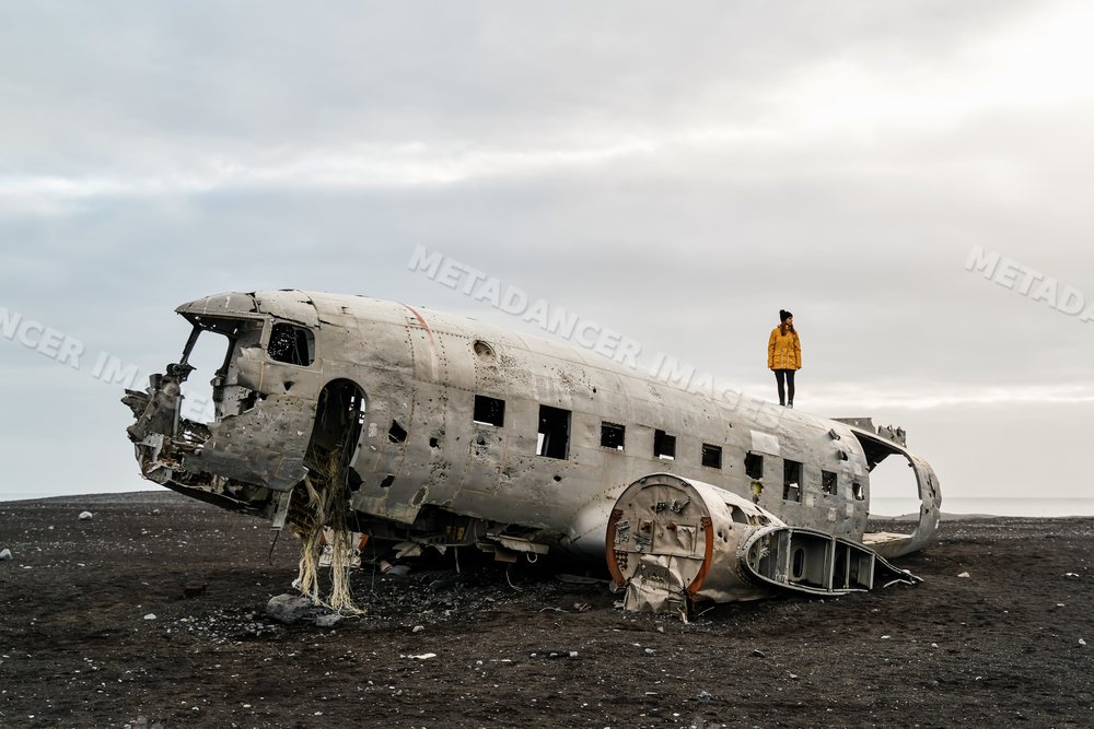 White Woman standing on abandoned airplane wreckage on black sand