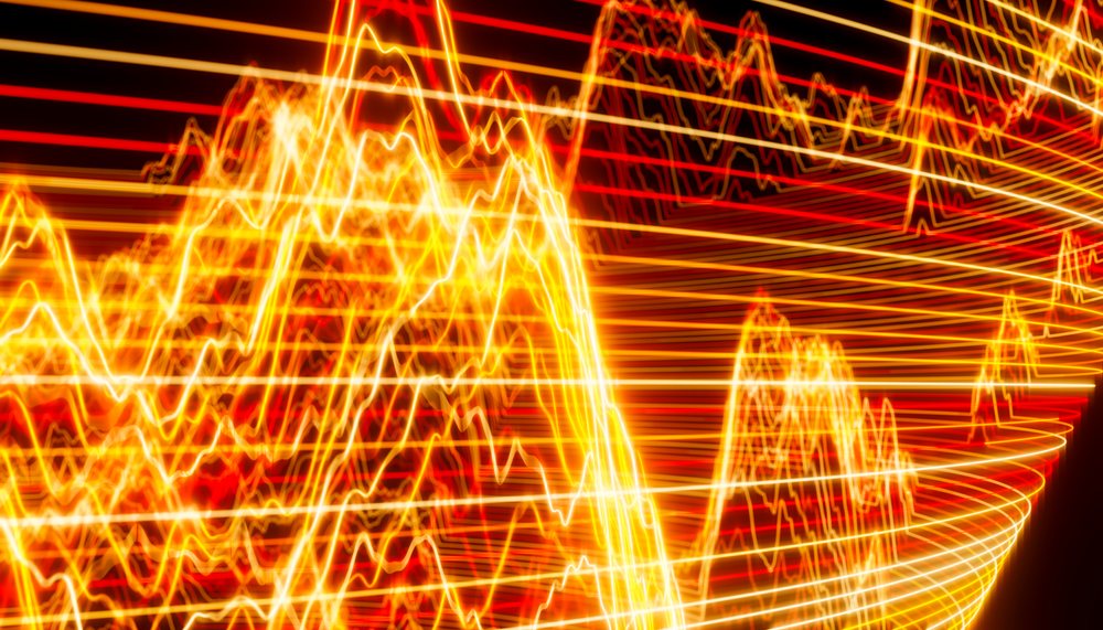 Abstract vibrant light trails with orange, red, and yellow colors forming dynamic energy waves on a dark background.