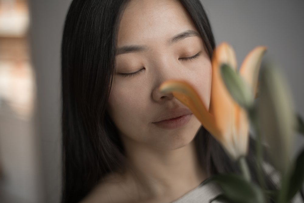 Woman with closed eyes holds a lily flower indoors, creating a calm and emotional portrait.